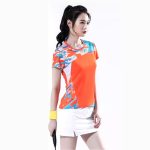 Women's orange badminton t-shirt with printed accents and white skirt for court sports.