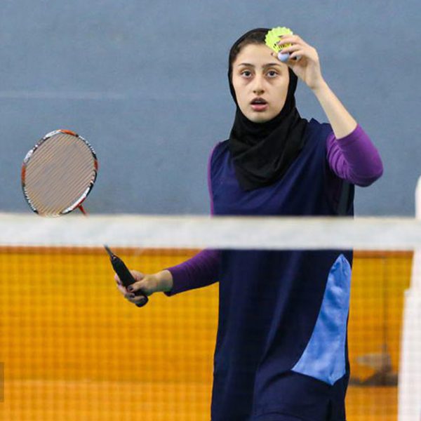 Hijab woman in navy blue and purple modest sportswear preparing to serve in badminton.